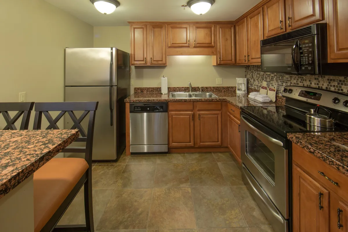 A view of an open-plan space featuring a modern kitchen island with stainless steel appliances, granite countertops, and warm wooden cabinetry. The layout flows naturally into a dining area, ideal for meals, family games, and socializing, with a welcoming ambiance that encourages gathering.