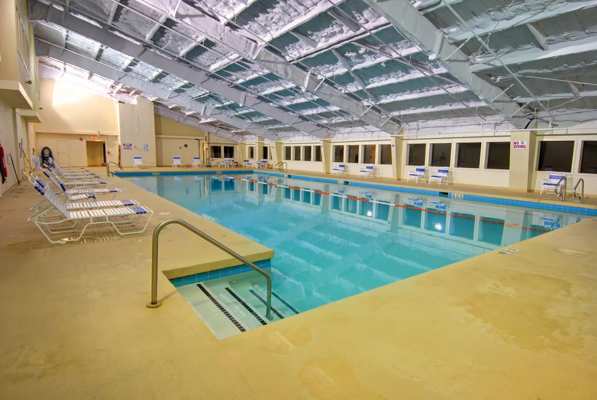 A spacious indoor swimming pool bathed in natural light from large windows. Lounge chairs line the pool, inviting relaxation. Several guests are swimming, while others chat poolside, creating a lively yet calming atmosphere perfect for unwinding or celebrating special moments.