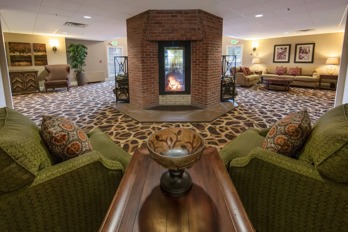 This image showcases a cozy brick fireplace as the focal point of a spacious living area, surrounded by comfortable seating and a decorative centerpiece. The arrangement invites guests to gather for conversations or relaxation, embodying the spirit of togetherness and comfort described in the section.