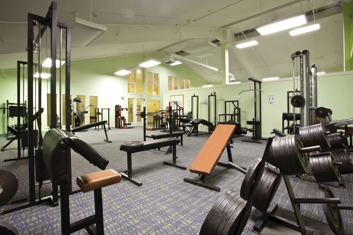 This image showcases a well-equipped fitness center featuring weightlifting equipment, exercise benches, and cardio machines. The space is designed for group activities, such as fitness classes and community challenges, with ample room for multiple people to work out together.